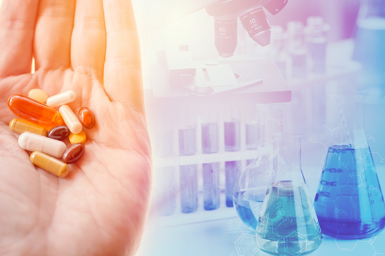 A hand holding some pills, a background with a microscope, test tubes and beakers