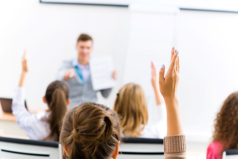 Students in a classroom raising their hands and engaging with the instructor