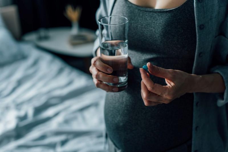 Pregnant women holding a glass of water and a pill, thinking if she should take the pill.